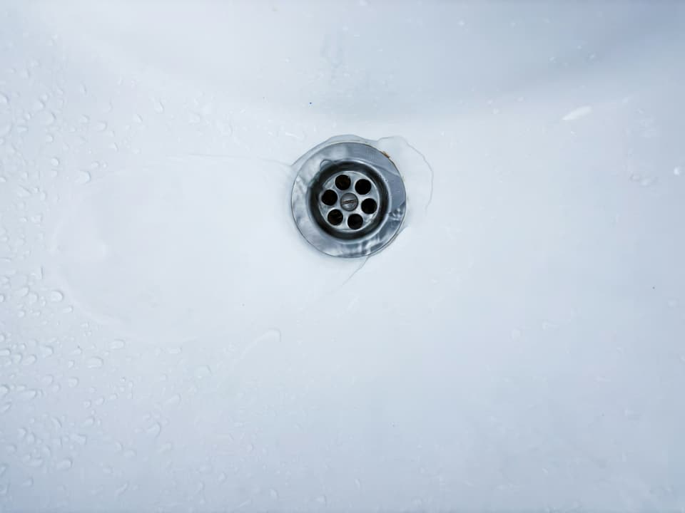 A metal drain in a wet white sink basin