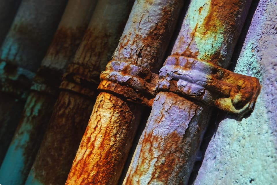 Rusted, flaking metal pipes held to a wall by corroded clamps