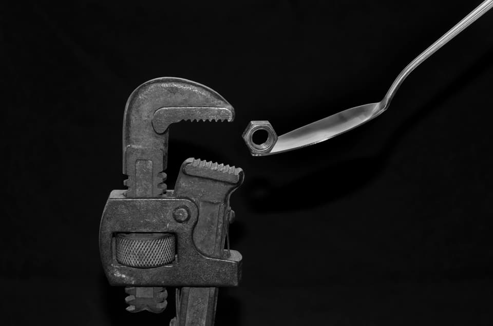 A pipe wrench beside a hex nut held on a spoon