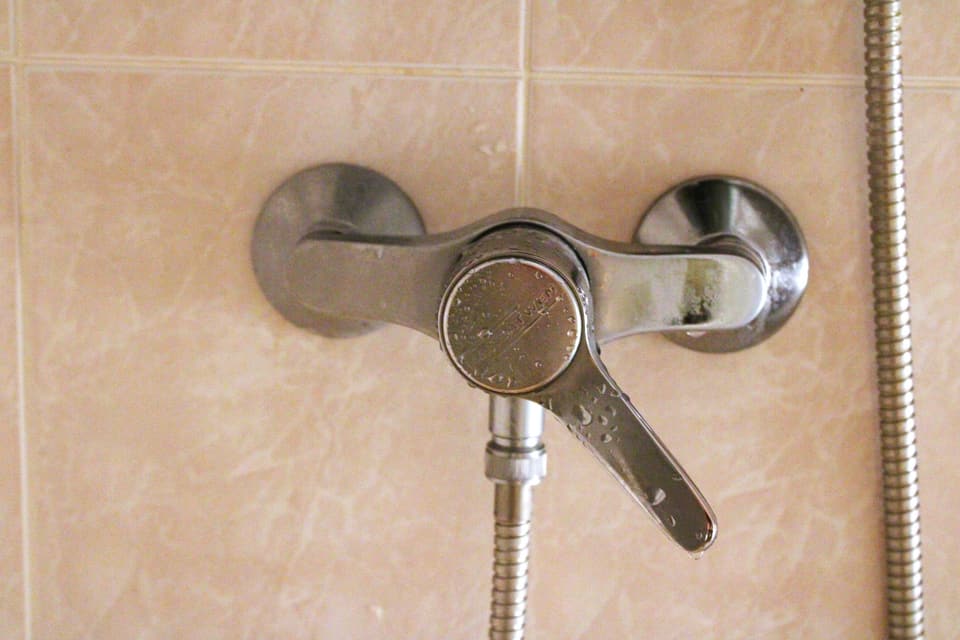 A wall-mounted shower mixer valve and hose on a tiled wall